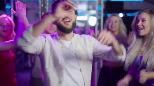 Danse active d'un bel homme caucasien barbu joyeux dans une boîte de nuit. portrait d'un millénium joyeux et confiant qui profite d'un concert le week-end avec un groupe d'amis à l'intérieur. Joie et divertissement. — Video