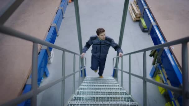 Brede opname van een geconcentreerde werknemer die op de ladder loopt in een stedelijk industrieel magazijn. Vooraanzicht van jonge knappe blanke man loopt boven in hardware bergplaats binnen. — Stockvideo