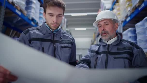 Geconcentreerde serieuze mannen die papierwerk onderzoeken en plannen bespreken die binnen in het magazijn staan. Professionele jonge en senior Kaukasische werknemers praten planning scheepvaart. Logistieke sector, — Stockvideo