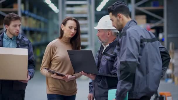 Serios hombres y mujeres de Oriente Medio y el Cáucaso discutiendo la logística como cargador de almacén que pasa con caja pidiendo detalles. Colaboradores profesionales hablando de planificación entrega de carga. — Vídeo de stock