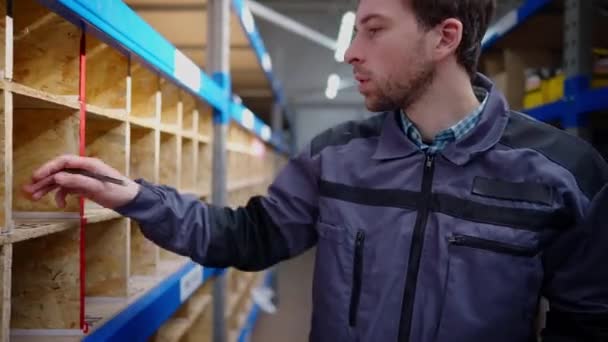 Jeune travailleur caucasien marchant dans l'entrepôt de quincaillerie vérifier les marchandises. Brunette bel homme contrôlant la disponibilité des stocks dans l'entrepôt. Concept de trading et de marchandisage. — Video