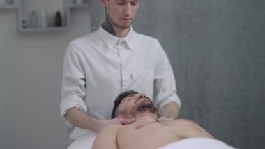 Masaj yatağında uzanmış yakışıklı beyaz bir adam. Ağır çekimde boyun kaslarına masaj yapan erkek masör gibi. Kapalı gözlerle rahatlamış bir müşteri. Kapalı kaplıcada terapi masajının keyfini çıkarıyor..