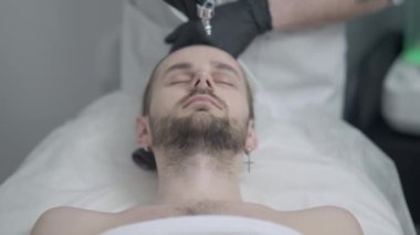 Kapalı gözlerle uzanan yakışıklı genç adamın yakından çekilmiş portresi tanınmaz bir güzellik uzmanı olarak cildini buhar cihazıyla temizliyor. Kafkas erkek müşteri güzellik salonunda gençleştirme işlemi yapıyor..