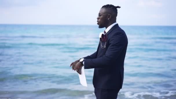 Troubled nervous African American businessman tearing documents standing on Mediterranean sea coast. Stressed handsome man ripping papers in slow motion. Despair and bankruptcy concept. — Stock Video