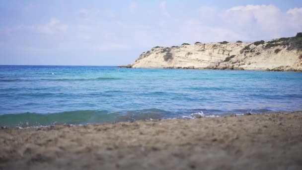 Amplo tiro de claras ondas azuis azuis azuis do mar Mediterrâneo rolando na praia de areia com rochas ao sol no fundo. Bela paisagem no resort de verão ao ar livre. Beleza do conceito de natureza. — Vídeo de Stock