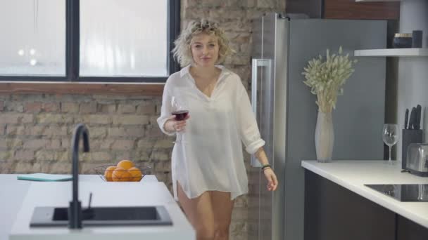 Superbe femme mince tatouée marchant avec un verre de vin dans la cuisine dansant et souriant. Portrait de heureuse dame caucasienne positive détendue s'amusant profiter des loisirs à la maison à l'intérieur. Mouvement lent. — Video