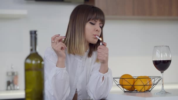 Střední záběr portrét štíhlé krásné mladé ženy, která si doma zapaluje cigaretu v kuchyni. Smutný kavkazský mileniální člověk s lahví vína uvnitř přemýšlí. Zpomalený pohyb. — Stock video
