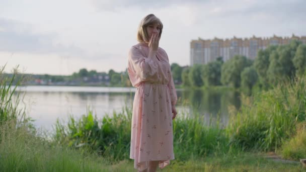 Retrato de tiro largo de mulher transexual coquete confiante em pé no prado verde no lago enviando beijo de ar olhando para a câmera sorrindo. Positivo caucasiano transgênero pessoa posando ao ar livre. — Vídeo de Stock