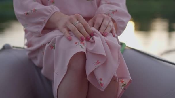 Nerozpoznatelná transvestita upravující růžové šaty na kolenou, sedící na člunu u u jezera. Dospělý kavkazský non-binární osoba odpočívající venku v létě večer. Romantika a koncepce genderové identity. — Stock video