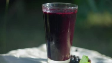 Güneş ışığında dışarıda dönen siyah frenk üzümü suyu ile yakın plan cam. Güneşli yaz bahçesinde sağlıklı organik vitamin içeceği.