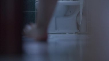 Çıplak ayaklı beyaz erkek bacakları tuvalet odasına giriyor külotlarını çıkarıyor ve ayaklarını yere vuruyor. Sabahları evdeki tuvaleti kullanan tanınmayan bir adam. Rutin ve hijyen kavramı.