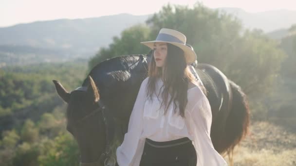 Sidovy av självsäker hästkvinna i halmhatt och graciösa djur promenader i solstrålar i sommar berg och lämnar. Vacker smal vit kvinna ryttare promenader med husdjur utomhus i solsken. — Stockvideo