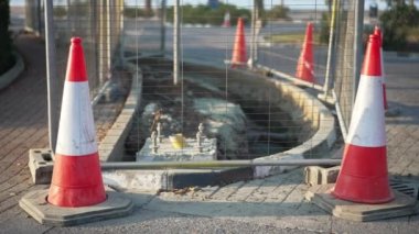 Kırmızı ve beyaz koni ve güneş ışığı altında yol yapımı. Endüstriyel şehir kaldırımı güneşli bir yaz gününde açık hava çukuruyla.