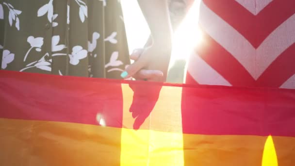Güneş ışınlarında el ele tutuşan, tanınmayan, yakından çekilmiş lezbiyen çift. Beyaz, LGBT 'li genç kadınlar gün ışığında ellerinde gökkuşağı bayrağı tutuyorlardı. Çeşitlilik ve hoşgörü kavramı. — Stok video