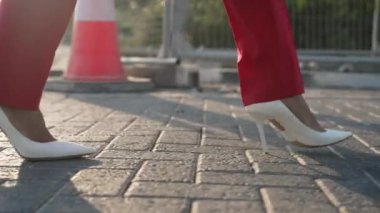 Canlı kamera, beyaz topuklu ayakkabılı şık bir iş kadını ve açık havada ağır çekimde kırmızı pantolonlu bir kadının adımlarını takip ediyor. Tanımlanamayan Kafkasyalı kadın yol inşaatı boyunca kasabada geziniyor..