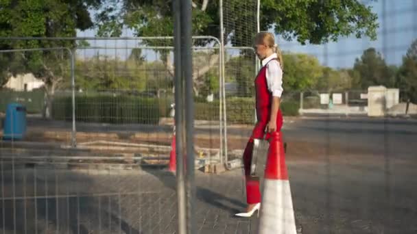 화창 한 날 도로 건설 현장을 걷고 있는 자신있는 사업가의 모습 이 눈에 띈다. 도시 밖에서 느리게 움직이고 있는우아 한 백인 여성의 넓은 샷. — 비디오