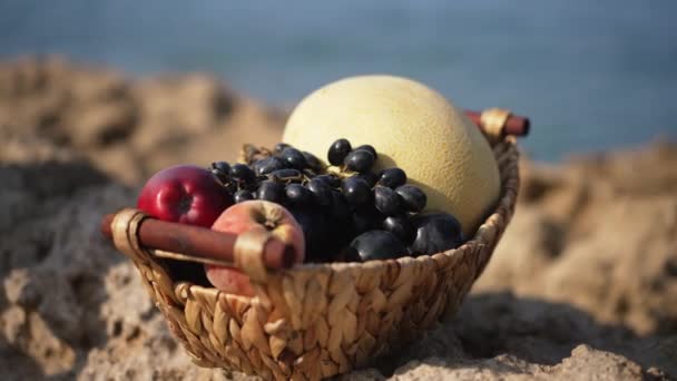 Close-up fruitmand in zonlicht met rennende mieren en schuimende zeegolven die op de achtergrond spatten. Lekkere heerlijke vitamine biologische appels druiven en meloen in de zon in de zomer resort. — Stockvideo