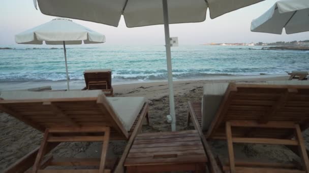 Weitwinkelige Landschaft mit türkisfarbenen Wellen des Mittelmeeres, die sich in Zeitlupe wälzen und Holzliegen, die vorne am Sandstrand stehen. Malerische Meereslandschaft im Sommerurlaub im Freien. — Stockvideo