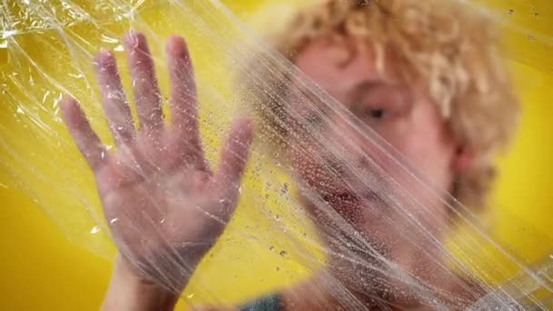 Zbliżenie męskiej białej ręki dotykającej mokrej folii z rozmazanym mężczyzną na żółtym tle. Świadomy młody aktywista pozujący z symbolem zmian klimatycznych i globalnego ocieplenia. — Wideo stockowe
