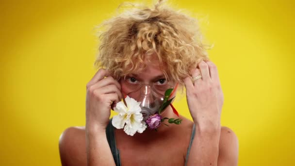 На передньому плані - портрет молодого кавказького дивака з квітами в масці небулізера. Редгед ЛГБТ людина з карими очима позує на жовтому фоні. Стиль і концепція різноманітності. — стокове відео