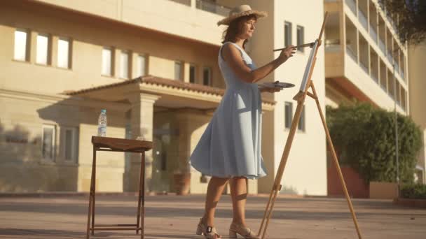 Amplio plano de talentosa mujer confiada pintando a la luz del sol al aire libre y saliendo. Delgado magnífico pintor caucásico alejándose en cámara lenta. Artes visuales y concepto de creatividad. — Vídeos de Stock