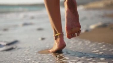 Canlı kamera, ince bronzlaşmış beyaz ayaklı, dövmeli Çinli bir kadının kum üzerinde ağır çekimde gün ışığında yürümesini takip ediyor. Akdeniz 'de gezinen tanınmayan genç bir kadının yakın çekim bacakları..