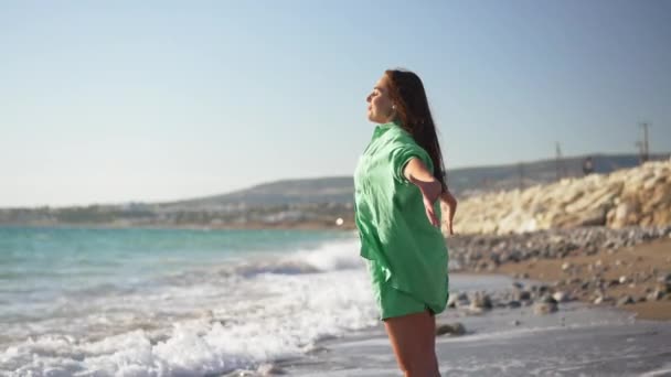 Vista lateral da jovem mulher feliz inalando ar fresco levantando as mãos admirando a beleza do mar Mediterrâneo pitoresco na praia de areia. Excitada bela turista caucasiano desfrutando de lazer em sol. — Vídeo de Stock