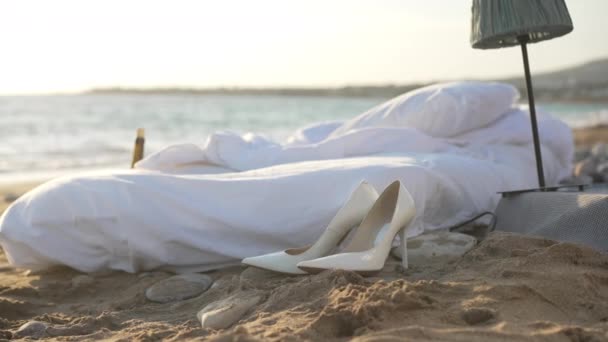 Amplio tiro blanco acogedora cama suave en la playa de arena con olas azules del mar Mediterráneo rodando en el fondo en cámara lenta. Cómodo colchón acolchado y tacones altos en el sol al aire libre en la costa del océano. — Vídeo de stock