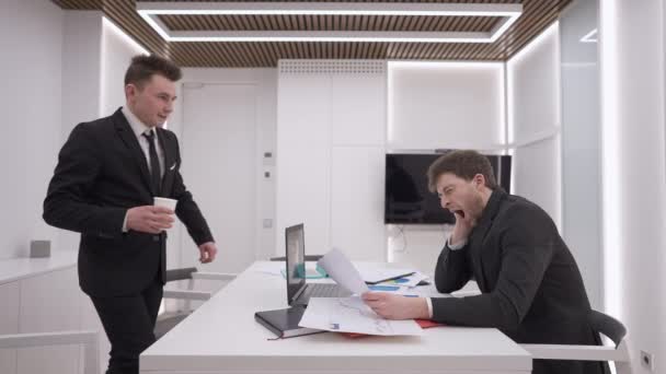 Kaukázusi férfi kávét hoz a túlhajszolt kollégának, aki laptoppal gondolkodik. Oldalnézet portré pozitív munkatársak támogató egymást az irodában. Lassú mozgás.. — Stock videók