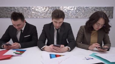Üç konsantre çalışan masada oturmuş akıllı telefonlara mesaj atıp yavaş çekimde konuşuyorlar. Kendine güvenen beyaz erkek ve kadının portresi. İnternet üzerinden iş görüşmeleri..