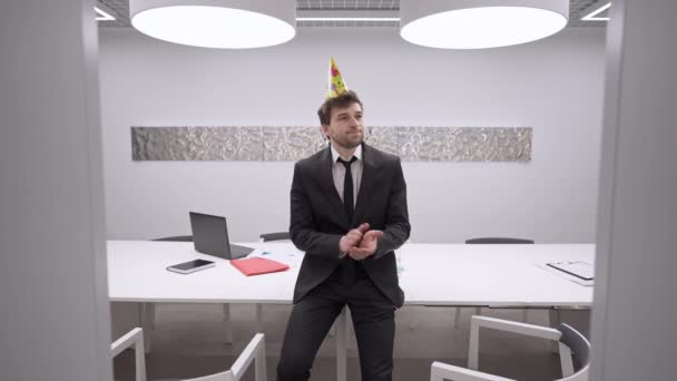 Hombre caucásico decepcionado en traje sentado en la oficina solo en el aplauso de cumpleaños hablando con expresión facial insatisfecha quitándose el sombrero de fiesta en cámara lenta. Retrato de triste empleado solitario en el interior — Vídeos de Stock