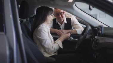 Heyecanlı bir eşle konuşan kocanın portresi. Arabada, sürücü koltuğunda anahtarla oturuyor. Bayilikten bayanlara yeni bir araba alan beyaz bir adam. Yavaş çekim.