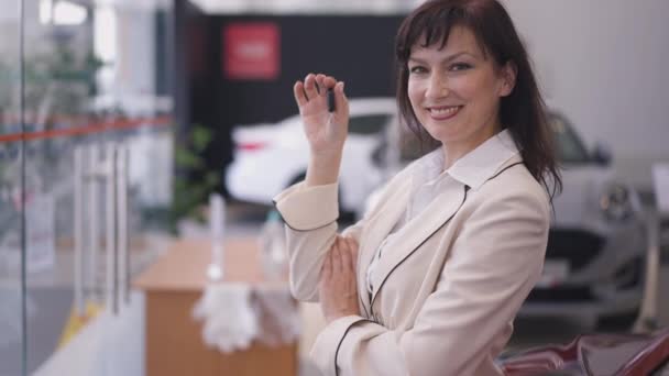 Leende vacker vit kvinna köpare skryta bil nyckel står i återförsäljare tittar på kameran. Porträtt av lycklig vuxen framgångsrik stolt kvinna poserar i auto showroom köpa ny bil. — Stockvideo