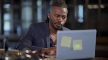 Restoran barında oturmuş internette internette sörf yapan özgüvenli Afro-Amerikan yakışıklı bir adamın portresi. Modern teknolojiler ve uzaktan çalışma kavramı.