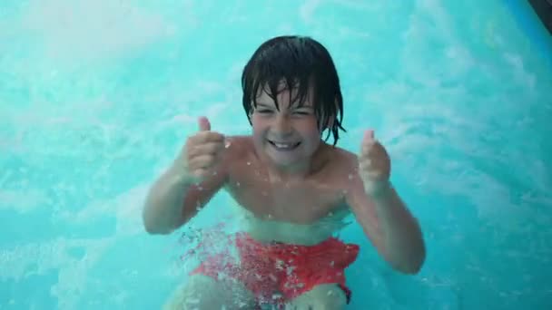 Ragazzo allegro che mostra i pollici verso l'alto sorridente guardando la fotocamera in piedi in acqua blu azzurro bollente in piscina. Ritratto di bambino caucasico felice iperattivo in posa all'aperto durante le vacanze estive. — Video Stock