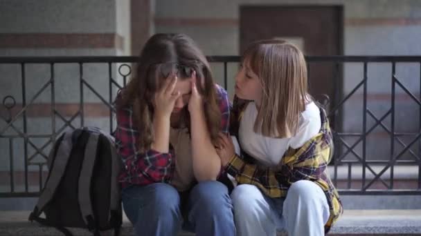 Front view portrait of empathetic teenage girl calming down friend crying sitting outdoors. Supportive Caucasian girl endorsing classmate bullied in school. Lifestyle and adolescence. — Stock Video