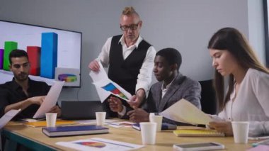 Ciddi bir patronun portresi çalışan konuşmasına evrak dağıtıyor. Güvenilir erkek CEO Afrika kökenli Amerikalı Orta Doğulu ve Kafkasyalı çalışanlarla ofis toplantı odasında fikir tartışıyor..