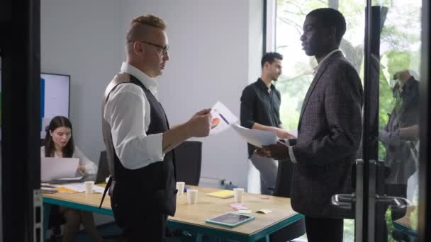 Zelfverzekerde blanke CEO steunt nieuwe Afro-Amerikaanse werknemer die praat en handen schudt. Side view van vriendelijk welkom in het kantoor in big business bedrijf. Succes en leefstijlconcept. — Stockvideo