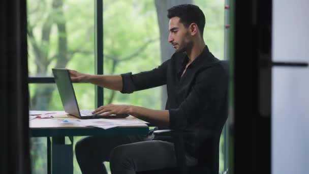 英俊自信的年轻人靠着椅子思维在笔记本电脑上查电子邮件的肖像。中东商人职业规划战略在室内办公.成功概念. — 图库视频影像
