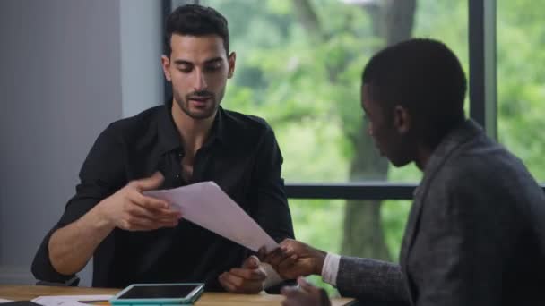 Midden-Oosten CEO en Afro-Amerikaanse manager schudden handen zittend in het kantoor analyseren strategie idee papierwerk. Dankbare knappe man bedankt professionele expert voor het werk praten brainstorming. — Stockvideo