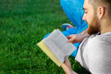 Genç adam parkta kitap okuyor.