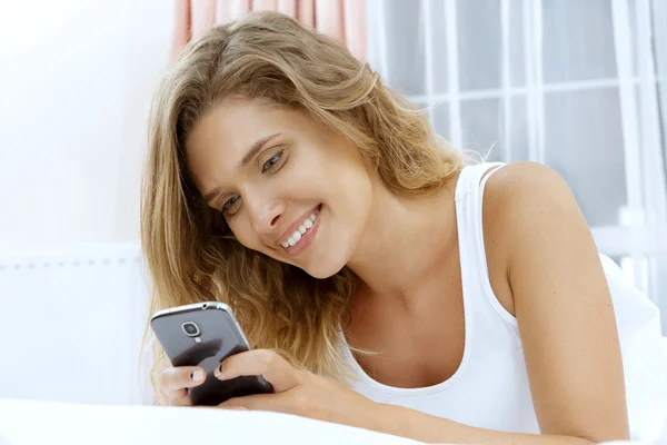 Joven hermosa mujer acostada en la cama con su teléfono — Foto de Stock
