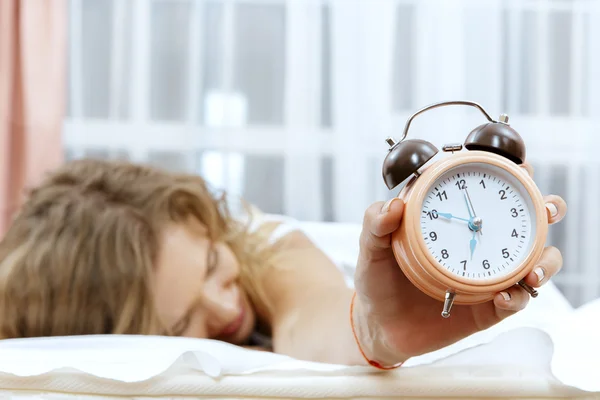 Mujer joven con despertador en la cama . — Foto de Stock