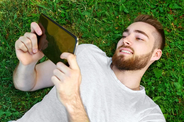 Junger Mann liegt mit Tablet im Gras im Park — Stockfoto