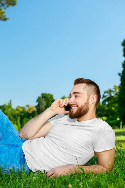 Jonge man liggen op het gras in park met telefoon — Stockfoto