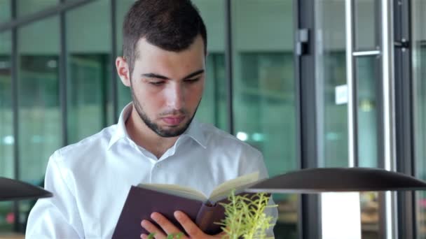 Joven en la cafetería leyendo un libro — Vídeos de Stock