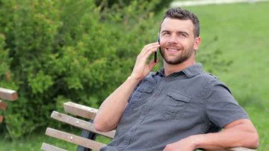 Parkta oturan adam cep telefonu üzerinde konuşurken