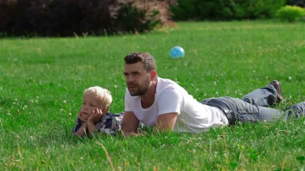 Pai e filho deitados na grama no parque — Vídeo de Stock