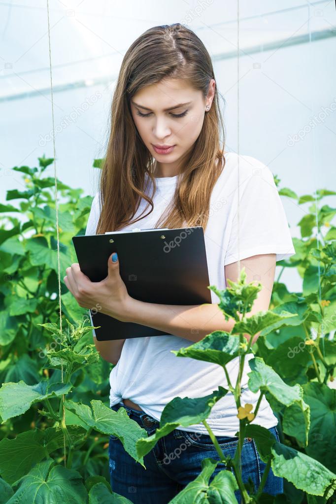Girl with clipboard takes notes and considers rows of plants.