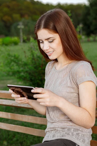 Retrato de una joven en el parque de mensajes de texto en la tableta — Foto de Stock
